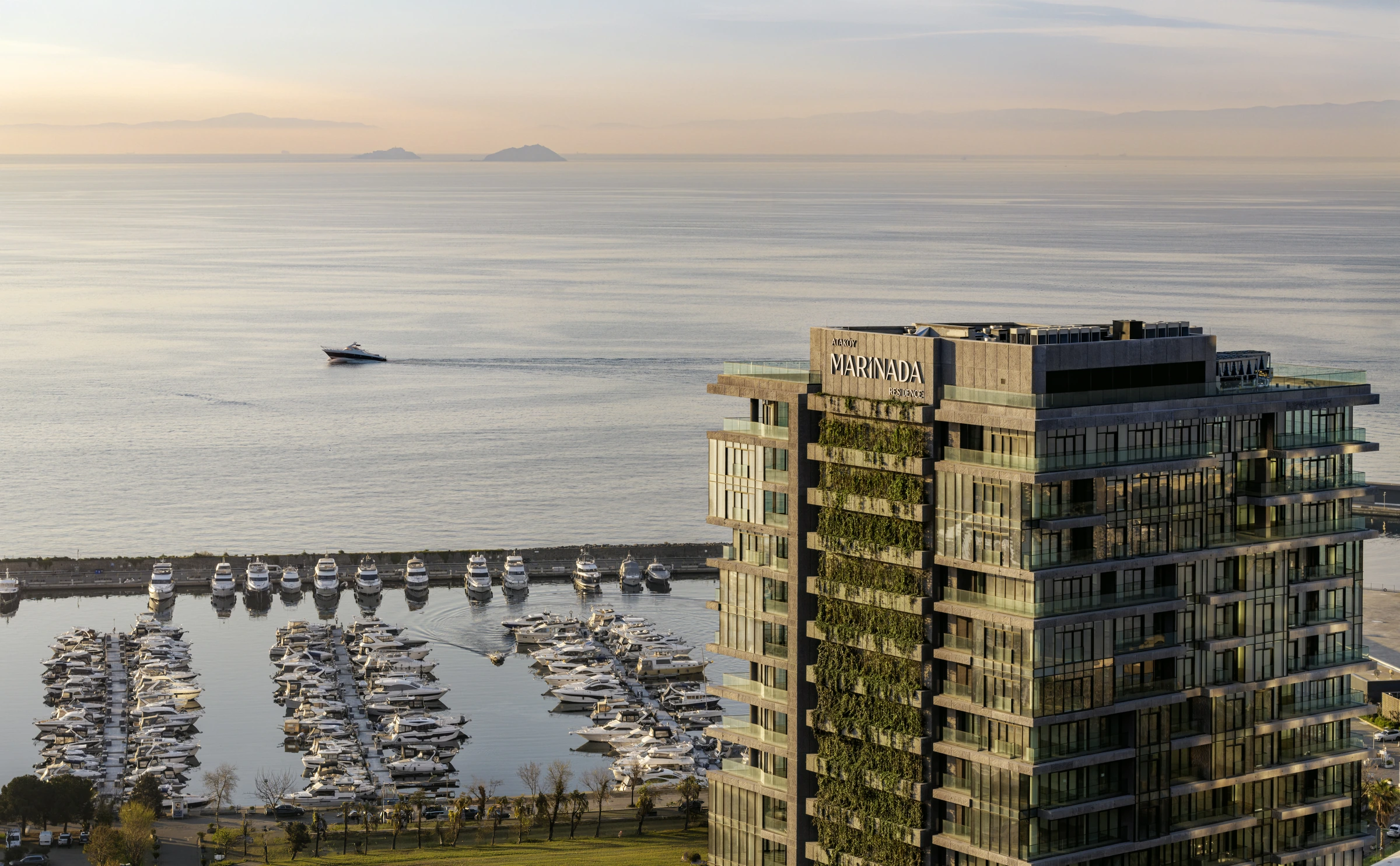 Gün batımında marinanın üzerinde yükselen Marinada Residence kulesi ve yeşil teraslı cephesi